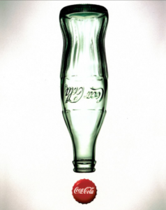 The Chesterman Company. An upside down glass Coca Cola bottle, empty with a metal Coca Cola cap below, making it look like an exclamation.