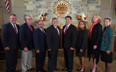 San Angelo Texas. A small group of people stand to pose for a photo in front of the seal for San Angelo on the wall.