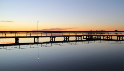 San Angelo Texas, a view of a pier on very smooth water with orange on the horizon.