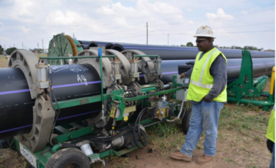 Wichita Falls. A worker with a bright vest and protective helmet uses a machine on a large pipe.