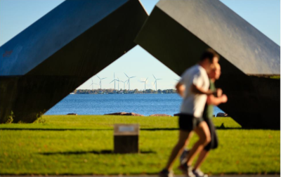 Kingston Ontario. Two joggers in a park out of focus with windmills across the water behind the joggers in focus.