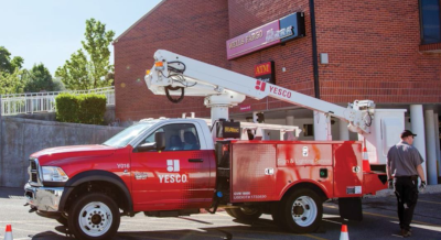 A Yesco truck with boom parked in front of a building and signage.
