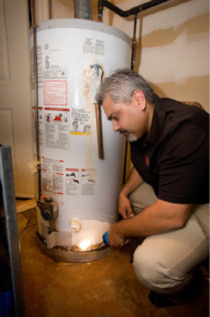 A Buyer's Choice Home Inspections employee kneels by a water heater with a flashlight, inspecting it.