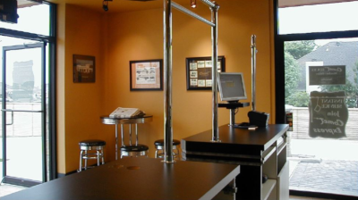 The inside front desk of a Comet Cleaners. Stools in the corner and a computer monitor on the counter.