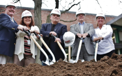 Enfield Connecticut, 5 people stand with hard hats on and holding shovels in a pile of dirt.