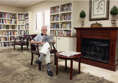 A man at Village on the Isle, sitting in a room with wood furniture and bookshelves on the wall behind him.