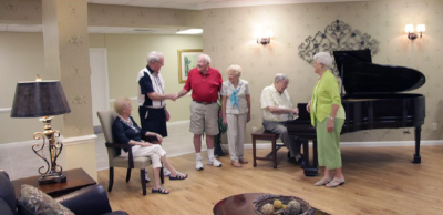 Village on the Isle, residents meet and enjoy piano playing by another resident in a living area.