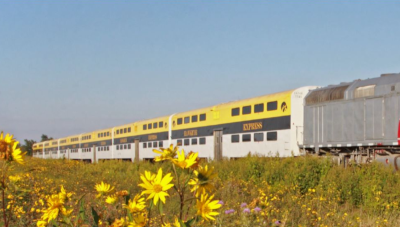 The Iowa Northern Railway Company train with Express cars going down the track with a green field and yellow flowers in front.