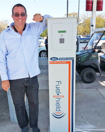 SCI Distribution. A man stands at a device at a gas station that says Fuel Shield.
