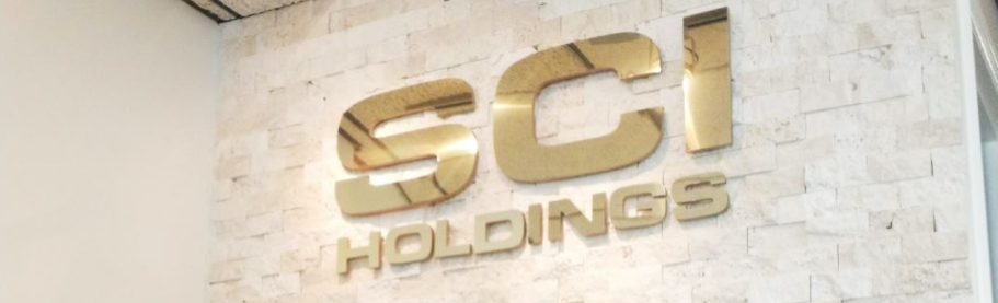 SCI Distributions. SC Holdings in gold lettering on a wall of light colored bricks.