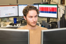 Customer Value Partners. A man works at a desk with computer screens in front of him and behind.