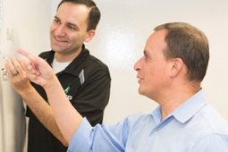 Customer Value Partners. Two men writing and pointing at a whiteboard on a wall.