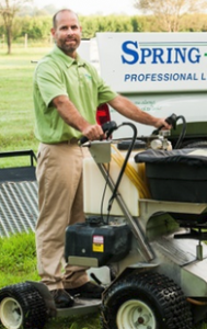 Spring-Green Lawn Care. A man standing on a lawnmower.