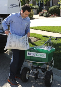 Spring-Green Lawn Care. A man putting bags of fertilizer on a Spring-Green spreading machine.