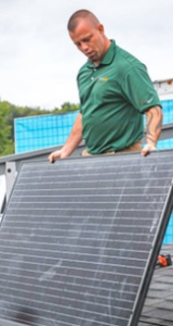 Werner Electric Ventures. A man holds a solar panel while on a rooftop.