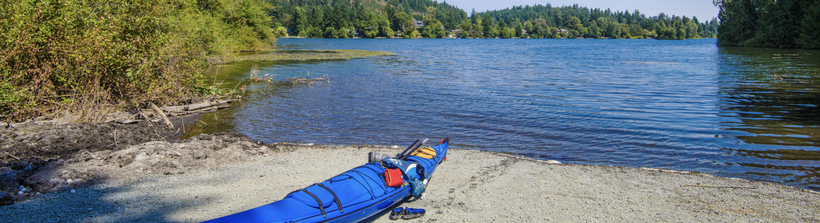 A kayak sitting on the beach in front of a lake with trees around the edges.