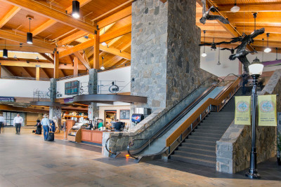 Bozeman Yellowstone International Airport inside showing shops, wood ceiling and an escalator and stairs.