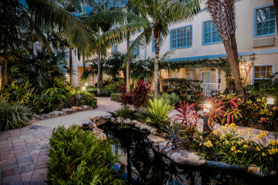 Futures of Palm Beach grounds showing a walkway outside with landscaping and trees and a building in the background.