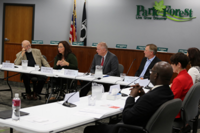 Park Forest Illinois meeting with people sitting around long tables. Each with a microphone and glasses of water.