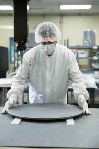 SQL Carbon LLC. A man carefully handling a wafer carrier in clean room conditions. He is wearing white clothing, gloves, hairnet and a face mask.