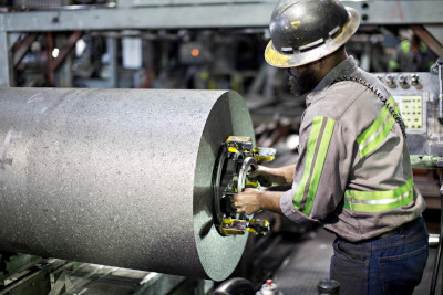 A Tokai Carbon employee wearing a reflective shirt and a hard hat attaches equipment to the end of a cylinder of carbon material.