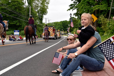 Coventry Connecticut, a family sitting on the roadside during a parade with firetrucks and horse in the road.