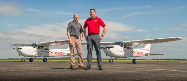 The Ohio State University Airport. Two men standing in front of two single engine airplanes.