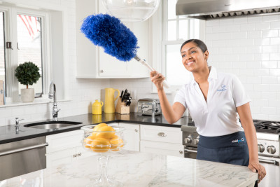 MaidPro employee dusting a light fixture in a kitchen.