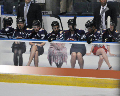 Signarama example of work. Hockey players sitting in the player box with a printed photo of the lower half of women sitting on a bench on the wall in front of the players.