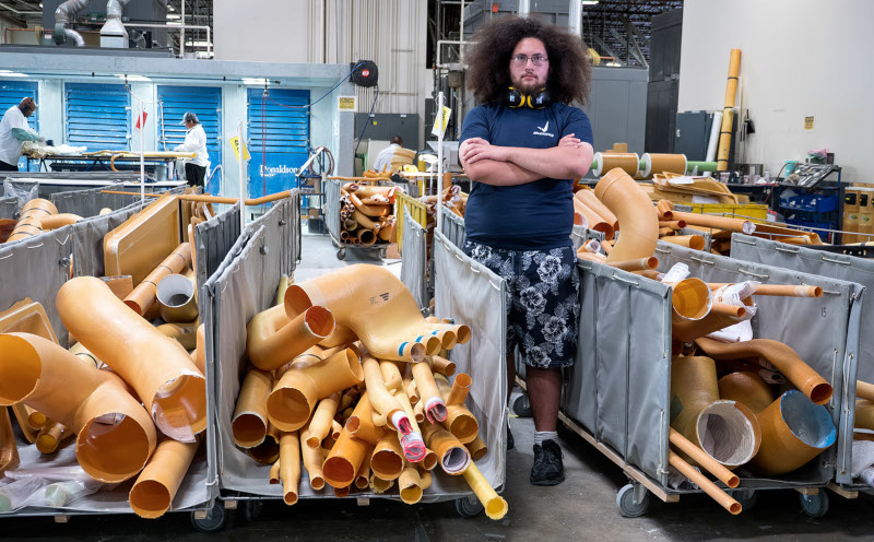 AIM Aerospace, worker standing between carts full of product with more people working behind in a large building.