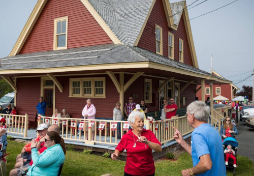 Cape Breton, Nova Scotia. Community event with people sitting and standing on building porches, in the grass and elsewhere.