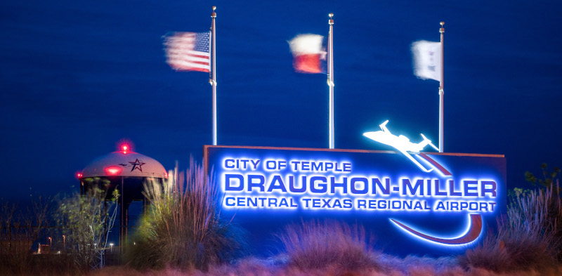 Daughon-Miller Central Texas Regional Airport sign lit up at night with flags above it blowing.