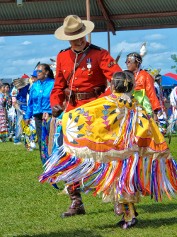 Wetaskiwin Alberta, powwow with colorful Native America Indian clothing and a small child dancing with a uniformed man.