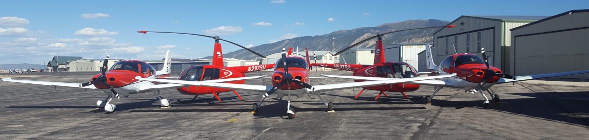 Cedar City Regional Airport. Three red and white airplanes and two red helicopters in a row on the tarmac.