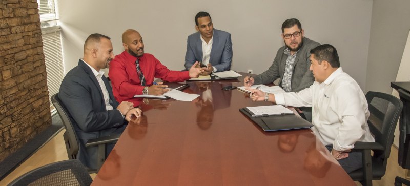 HNM Global Logistics. 5 men talking at a table in ties.