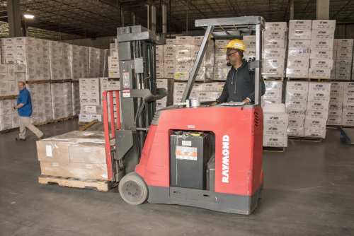 HNM Global Logistics. Warehouse with an employee moving a pallet with a forklift and another worker nearby.