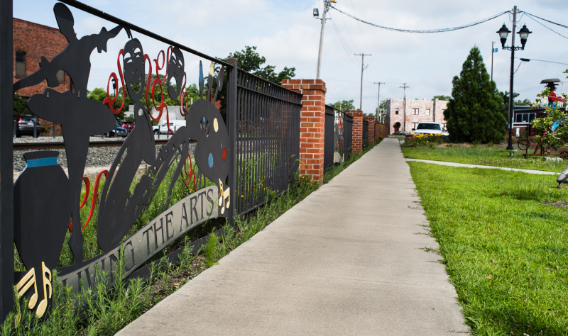 Kinston, North Carolina sidewalk with a metal fence that has Living the Arts on it with figures.