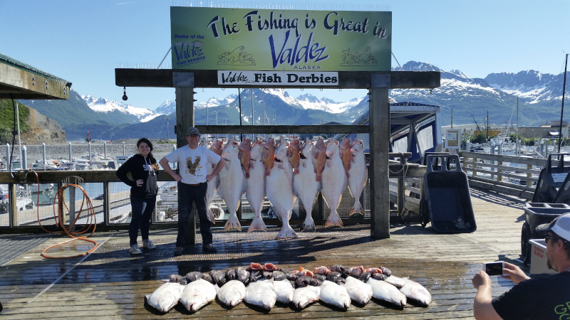 Port of Valdez fishing catch at the docks. Fished lined up on the ground and behind two people posing for the photo.
