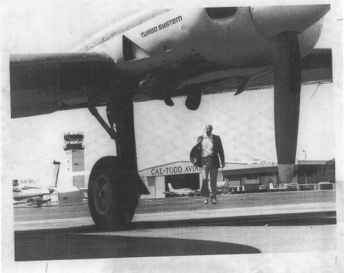 Redding Municipal Airport vintage photo of a man walking up to a plane with Turbo System written on the side and the airport behind him.