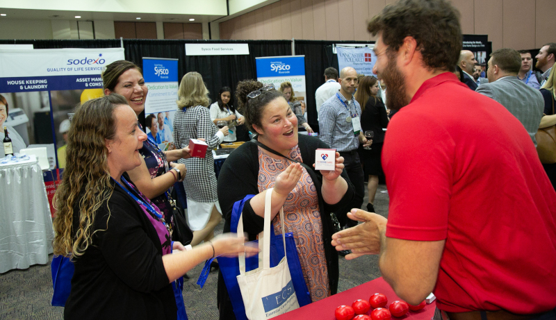 The California Assisted Living Association, event with vendors and a man talking to a few women who are laughing.