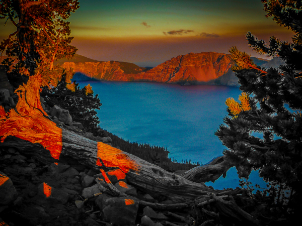 Klamath County, Oregon photo between some trees looking over a stump out into a body of water surrounded by mountains.