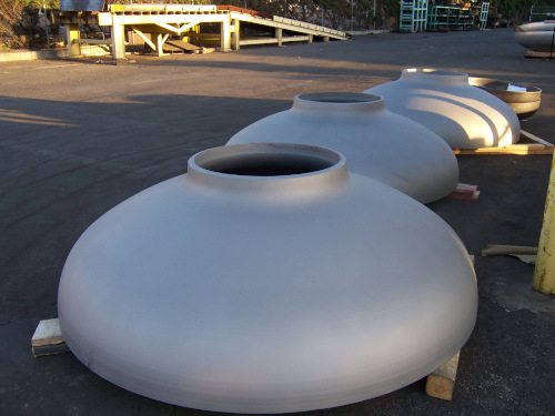 Commercial Metal Forming examples of work sitting on wood outside, three large round metal lids with a hole in the top.