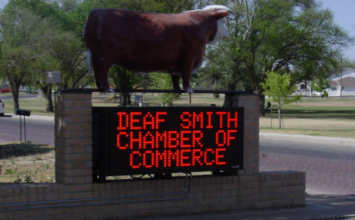 Deaf Smith County Texas Chamber of Commerce sign with red light lettering and a cow on top.