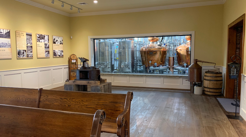 Louisiana Spirits / Gator Bites visitors center showing wooden benches and a glass window looking on at distillery equipment.