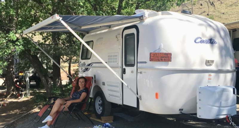 Casita Enterprises Inc., a woman sitting outside of her set up camper complete with awning.