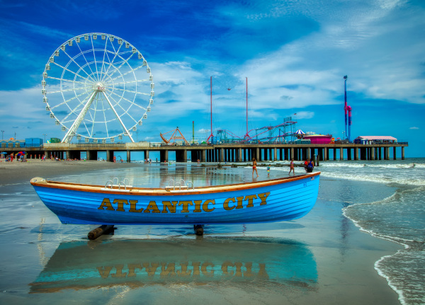 New Jersey Economic Development Authority Atlantic City from the beach looking at a blue boat on the sand with Atlantic City written on the side and the boardwalk with a Ferris wheel behind.