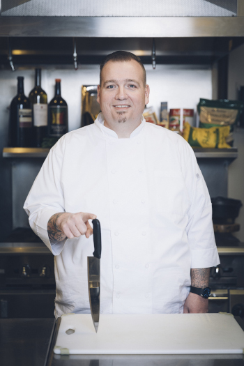 Overland Park Convention Center award winning chef posing for a photo holding a knife on the table upright with a finger on the handle.