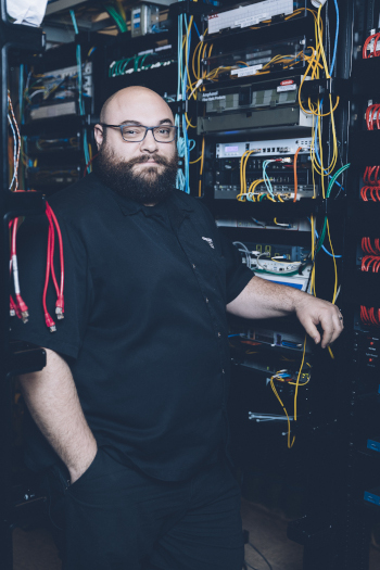 Overland Park Convention Center employee standing in an IT room next to computer equipment with wires.