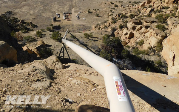 Peak Utility Services Group operating company Kelly Cable New Mexico job site showing pipes starting down a tall clif, towards a group of work trucks and employees very far below.