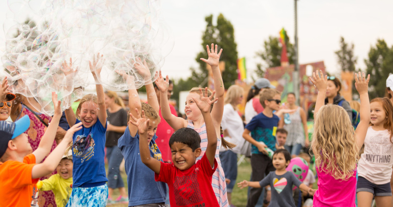 Dublin, California kids with large bubbles in the air and their eyes closed with hands up to pop them.